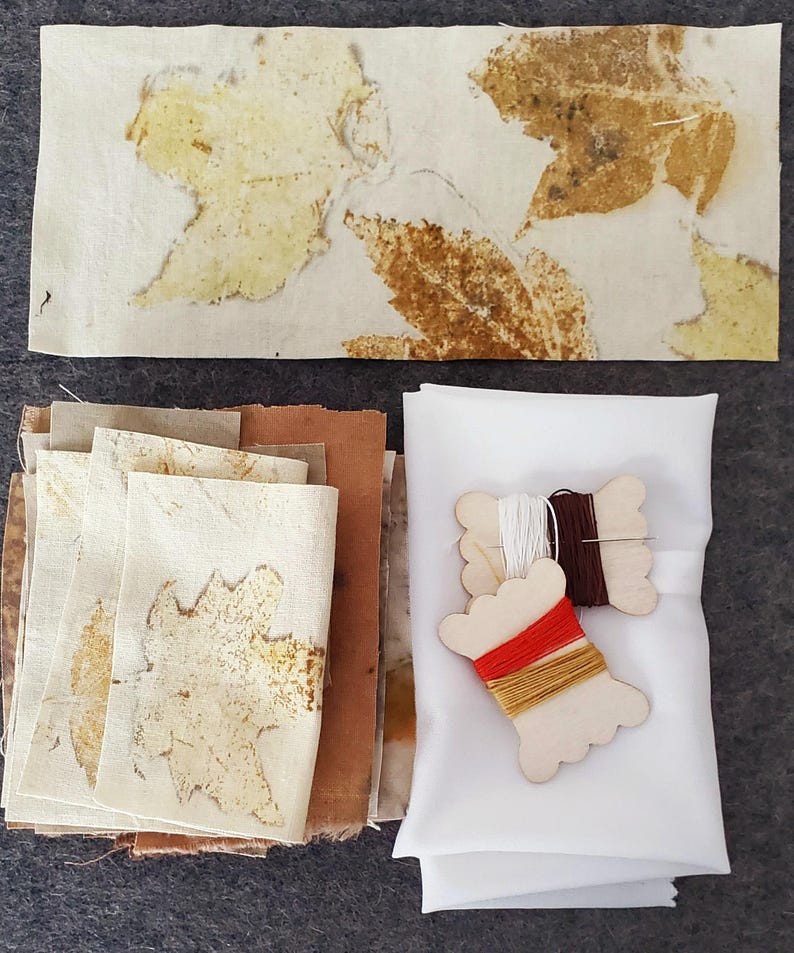 May include: A set of fabric squares with leaf patterns in shades of brown and beige, along with white fabric and spools of red, brown, and yellow thread.