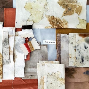 May include: A collection of fabric squares with various shades of brown, beige, and orange. Some squares have leaf patterns, while others have a speckled or mottled appearance. The fabric squares are arranged on a gray surface. The text "THIS SIDE UP" is visible on a white label.