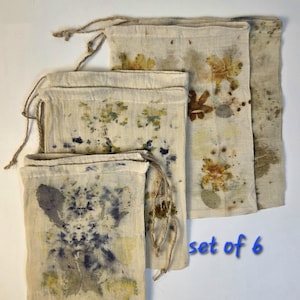 May include: A set of 6 off-white fabric drawstring pouches featuring botanical prints in shades of yellow, brown, blue, and green. Each pouch has a natural fiber cord closure and displays unique, organic plant-based patterns on the front surface.