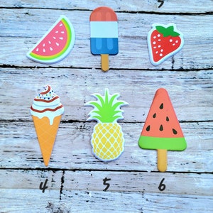 Puede incluir: Seis recortes de fieltro de temática veraniega, incluyendo una rodaja de sandía, helado, fresa, cono de helado, piña y una paleta de sandía.