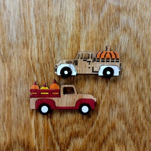 Può includere: Due camioncini giocattolo di legno, uno dipinto di rosso e l'altro di marrone. Entrambi i camioncini trasportano zucche.