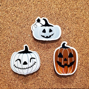 May include: Three Halloween-themed pumpkin stickers with different facial expressions. The stickers are white, brown, and orange with black details.