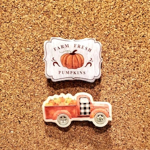 Puede incluir: Una camioneta roja con un diseño a cuadros blanco y negro en la parte trasera está llena de calabazas naranjas. La camioneta está sobre un fondo de corcho con un letrero que dice "Farm Fresh Pumpkins" con una sola calabaza naranja en él.