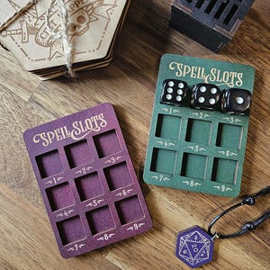 May include: Two wooden spell slot trackers, one green and one purple, with a set of black dice and a black and purple d20 necklace. The trackers have numbers 1-9 on each slot.
