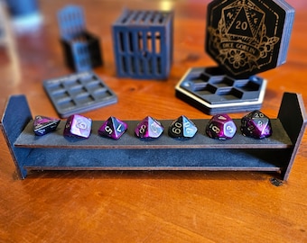 May include: A black wooden dice tower with a gold inscription that reads "Dice Goblin" and a black and purple dice tray with seven black and purple dice.