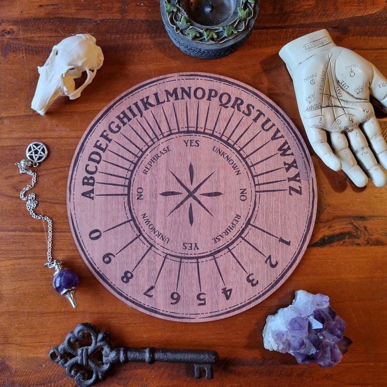 May include: A wooden Ouija board with a purple and white planchette, a purple crystal, a silver pendulum, and a key. The board has the letters of the alphabet, numbers 0-9, yes, no, goodbye, and unknown.