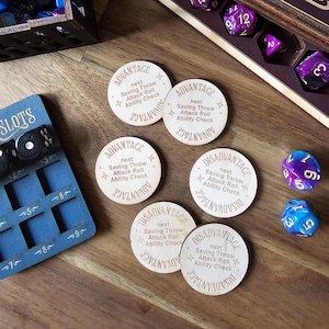 Puede incluir: Fichas de madera de Ventaja y Desventaja con texto grabado, junto con varios dados de múltiples caras. Se ve una bandeja de dados azul con ranuras para dados. Las fichas son circulares.