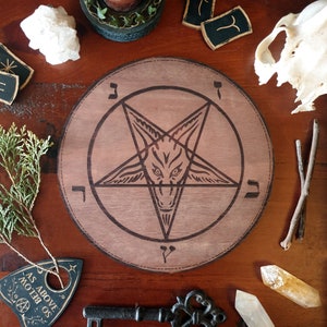 May include: A wooden pentagram with a goat's head in the center. The pentagram is surrounded by Hebrew letters. The board is brown and has a distressed look.