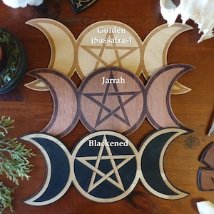 May include: Three wooden triple moon pentacles, one in golden (Sassafras) wood, one in Jarrah wood, and one in blackened wood.