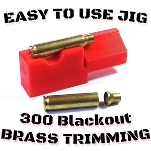 May include: A bright red 3D-printed plastic jig for 300 Blackout brass trimming. The jig features a molded cradle holding a brass cartridge case. Below the jig, a separate brass cartridge case and a small trimmed brass neck are visible.