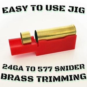 Może przedstawiać: Czerwony przyrząd z mosiężnym nabojem i mosiężnym pierścieniem. U góry tekst "EASY TO USE JIG", a na dole "24GA TO 577 SNIDER BRASS TRIMMING". Przyrząd przeznaczony jest do przycinania mosiądzu.