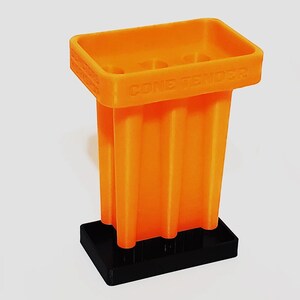 May include: An orange plastic "Cone Tender" with a black base. The product has a rectangular top with three holes and a series of vertical, ribbed supports. The text "CONE TENDER" is printed on the side.