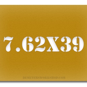 May include: Mustard-colored stencil with the text "7.62X39" cut out in white. The text is in a bold, sans-serif font. The website address "DEMETERSWORKSHOP.COM" is at the bottom.