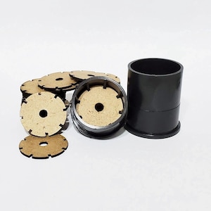 May include: A collection of laser-cut wooden discs with a central hole and notched edges, alongside a black cylindrical container. The discs are stacked and scattered, suggesting a crafting or organizational theme.