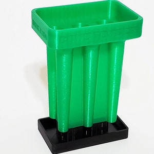 May include: A bright green 3D-printed pen holder with a rectangular top and a black base. The pen holder has a series of vertical, cylindrical supports. The text "POWER TENNER" is printed on the side.