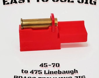 Puede incluir: Una plantilla roja para recortar latón con un cartucho de latón en su lugar. El texto "EASY TO USE JIG" está en la parte superior y "45-70 to 475 Linebaugh BRASS TRIMMING JIG" en la parte inferior. La plantilla está diseñada para recortar casquillos de latón.