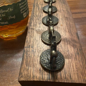May include: A wooden barrel stave with eight metal bottle stoppers featuring a horse and rider design. The stoppers are arranged in a row on the stave. The stave is a dark brown color and has a rough texture. The stoppers are a shiny gold color.