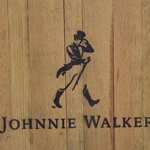 May include: A round wooden sign with the Johnnie Walker logo. The logo features a man in a top hat and walking stick, with the text "JOHNNIE WALKER." printed below.