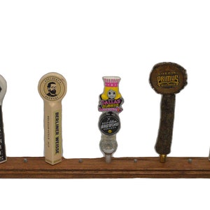 May include: Five different beer tap handles on a wooden rack. The handles are all different colors and designs. The handles are labeled "Oasis Pub Series", "Auldbrass Brewery Berliner Weisse", "Deep Ellum Brewing Dallas Blonde", "Live Oak Brewing Primus", and "Oasis Pub Series".