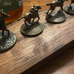 May include: A set of five miniature horse and jockey bottle stoppers, each with a different pose, on a wooden base. The stoppers are made of metal and have a gold finish.