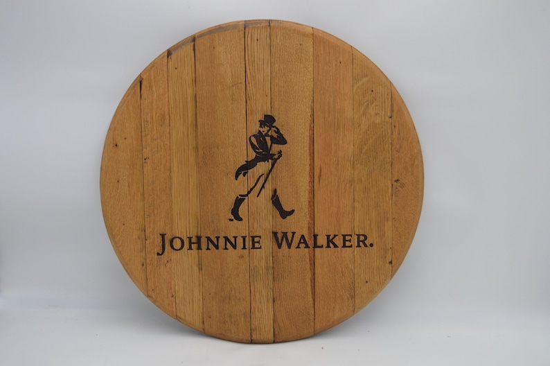 May include: A round wooden sign with the Johnnie Walker logo. The logo features a man in a top hat and walking stick, with the text "JOHNNIE WALKER." below.