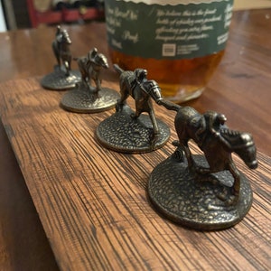 May include: Four miniature bronze horse bottle stoppers with jockeys on their backs. The stoppers are arranged in a row on a wooden surface.