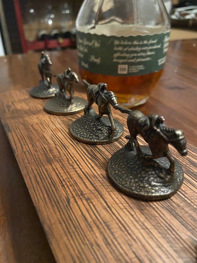 May include: Four miniature bronze horse bottle stoppers with jockeys on their backs. The stoppers are arranged in a row on a wooden surface.