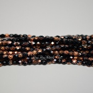 May include: A strand of black and copper metallic glass beads. The beads are faceted and have a textured surface.