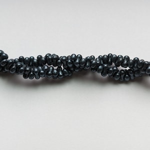 May include: A strand of dark gray beads, arranged in a wavy pattern on a white background.