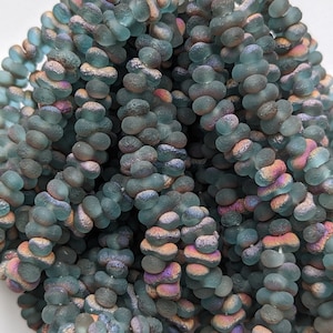 May include: A strand of iridescent blue glass beads with a textured, irregular shape. The beads have a frosted finish and a subtle shimmer.