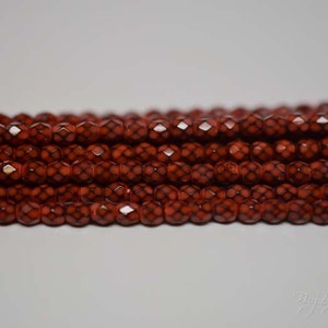 May include: A strand of red glass beads with a geometric pattern. The beads are faceted and have a shiny finish.