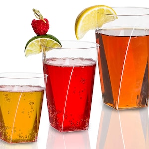 May include: Three clear plastic cups with different colored drinks. The cup on the left has a yellow drink, the middle cup has a red drink, and the cup on the right has an orange drink. The cups are all on a white background.