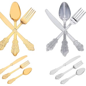 May include: Two sets of gold and silver cutlery, each set includes a fork, knife, and spoon. The cutlery has an ornate design and is arranged in a criss-cross pattern.