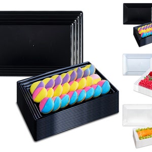 May include: A set of black and clear plastic serving trays. The black trays are stacked and filled with colorful cookies. The clear trays are stacked and filled with fruit and candy.