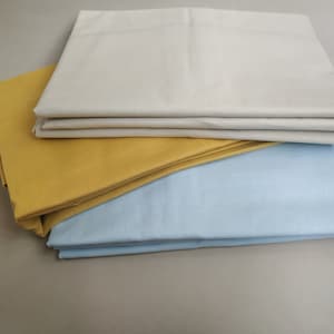 May include: A stack of three folded fabric sheets in different colors: light beige, mustard yellow, and light blue.