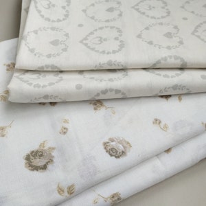 May include: Three pieces of white fabric with different patterns. The top fabric has a gray heart pattern, the middle fabric has a gray floral pattern, and the bottom fabric has a brown floral pattern.