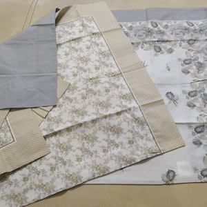 May include: Three fabric squares with floral patterns. The top square is gray with a white floral pattern. The middle square is white with a beige floral pattern and a gray border. The bottom square is white with a gray floral pattern and a beige border.