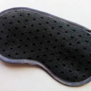 Puede incluir: Una máscara para dormir negra con ribete de satén gris y un patrón de puntos.