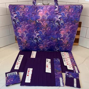 May include: A purple tote bag with a marbled pattern featuring pink and blue swirls, accompanied by matching purple fabric card holders and organizers. The set includes multiple playing cards inserted into the slots, displaying various suits and ranks.