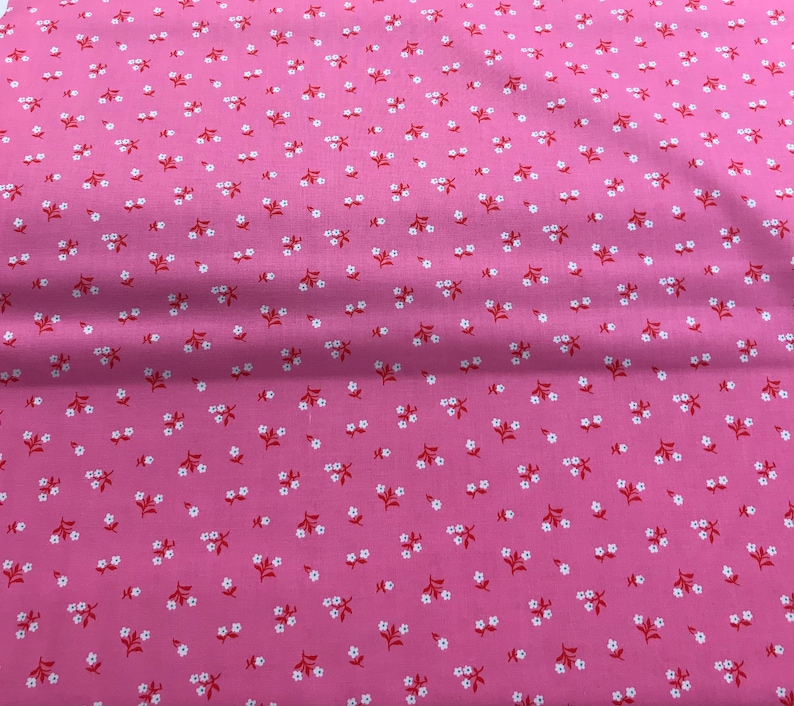 May include: Pink fabric with a white and red floral pattern. The fabric is a solid pink color with small white flowers and red stems.