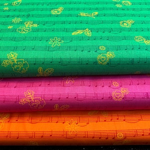 Può includere: Tre campioni di tessuto con un motivo di note musicali e fiori. Il campione superiore è verde, il campione intermedio è rosa e il campione inferiore è arancione.