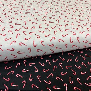 May include: Two rolls of fabric, one white and one black, feature a repeating pattern of red and white candy canes. The fabric is suitable for festive crafts or sewing projects, perfect for Christmas.