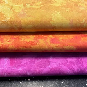 Könnte beinhalten: Drei Stoffmuster in einem Farbverlauf von Orange, Rot und Lila. Der Stoff hat eine marmorierte, strukturierte Oberfläche.