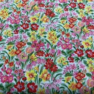 May include: A white fabric with a floral print featuring red, yellow, and pink flowers. The fabric is covered in a variety of flowers, creating a busy and colorful pattern.