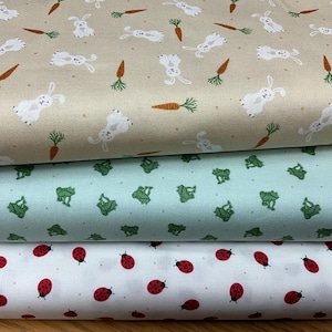 Puede incluir: Tres muestras de tela con diferentes patrones. La muestra superior es beige con conejos blancos y zanahorias naranjas. La muestra del medio es verde claro con ranas verdes. La muestra inferior es blanca con mariquitas rojas.