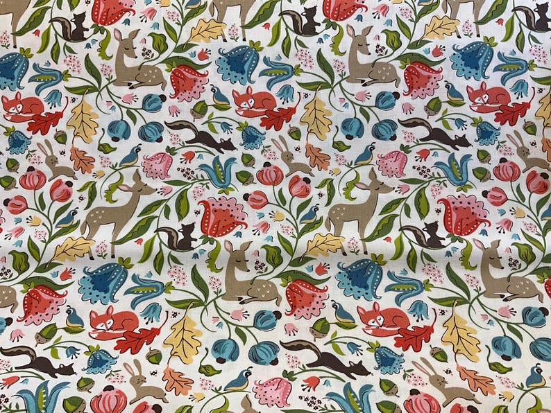 May include: White fabric with a repeating pattern of woodland creatures and floral elements. The design includes deer, foxes, squirrels, rabbits, and birds, along with flowers and leaves in shades of red, blue, pink, and yellow.