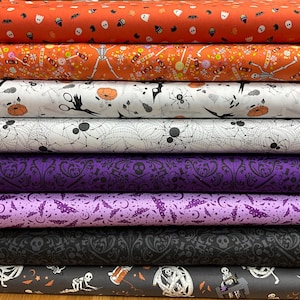 Peut inclure: Une pile de rouleaux de tissu sur le thème d'Halloween. Les tissus présentent divers motifs, notamment des squelettes, des araignées, des chauves-souris et des citrouilles, dans des couleurs comme l'orange, le blanc, le violet et le noir. Les tissus sont probablement en coton ou dans une matière similaire, adaptés à la couture.