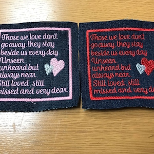 May include: Two embroidered patches on a dark blue denim background. The patches feature the same text in pink and red embroidery: "Those we love don't go away, they stay beside us every day. Unseen, unheard but always near. Still loved, still missed and very dear". Each patch has a heart design with a white outline.