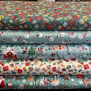 May include: Five stacked bolts of fabric featuring holiday patterns. The top bolt is dark green with colourful gift boxes. The second is light blue with snowmen. The third is light blue with houses and holly. The fourth is cream with gift boxes. The bottom is green with Santa, animals, and gifts.