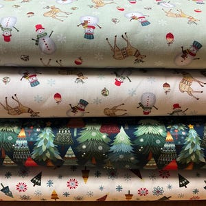 May include: Four stacked bolts of fabric featuring holiday patterns. The top two bolts show snowmen, reindeer, and ornaments on light green and cream backgrounds. The third bolt displays a dark blue forest of pine trees. The bottom bolt features small trees and snowflakes on a cream background.